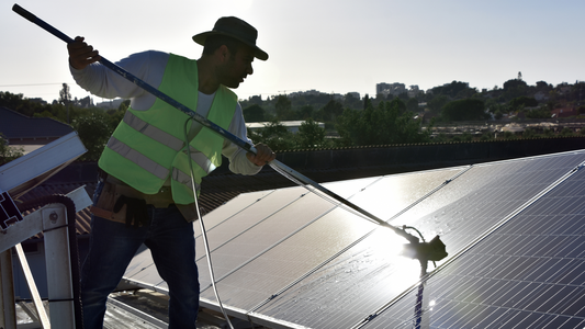 Man on a roof cleaning solar panels with a long-handled brush