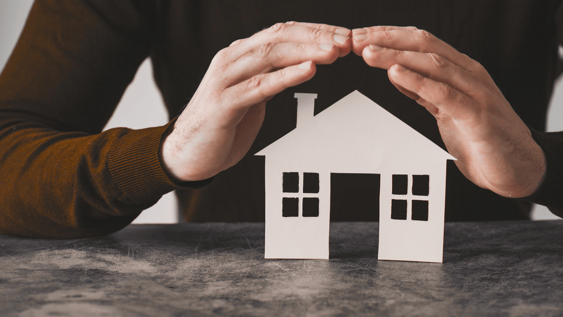 Hands held over a small home cutout, visualizing homeowner's insurance.